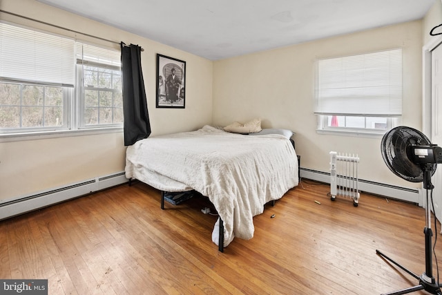 bedroom with hardwood / wood-style flooring, multiple windows, and baseboard heating