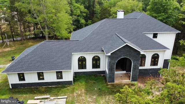 view of front of house with a shingled roof, a front yard, stone siding, and a chimney