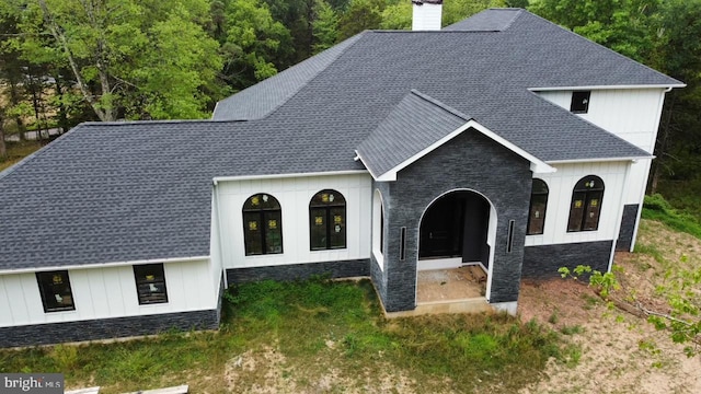 modern inspired farmhouse with stone siding, roof with shingles, and a chimney