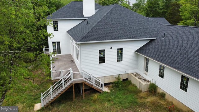 back of property featuring stairway, a chimney, and a shingled roof