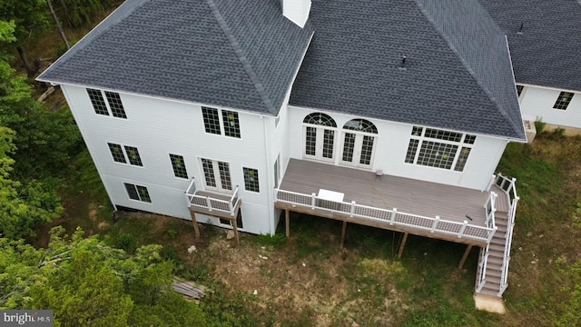 back of house featuring a chimney, a deck, and a shingled roof