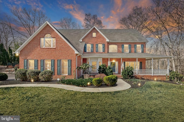 view of front of house with brick siding, a porch, and a front yard