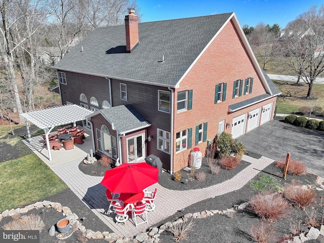 back of property featuring a shingled roof, a chimney, a yard, driveway, and a pergola