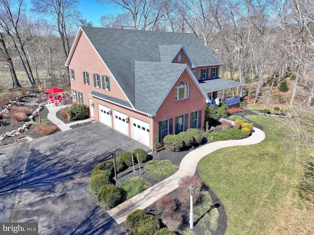 view of front of house featuring a front yard, driveway, a shingled roof, a garage, and brick siding