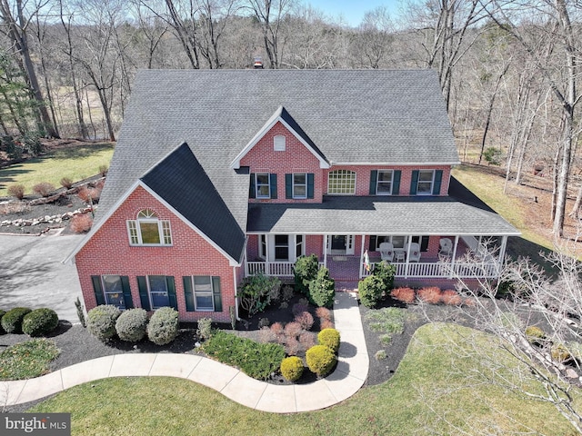 view of front of house with a front yard, brick siding, covered porch, and a shingled roof