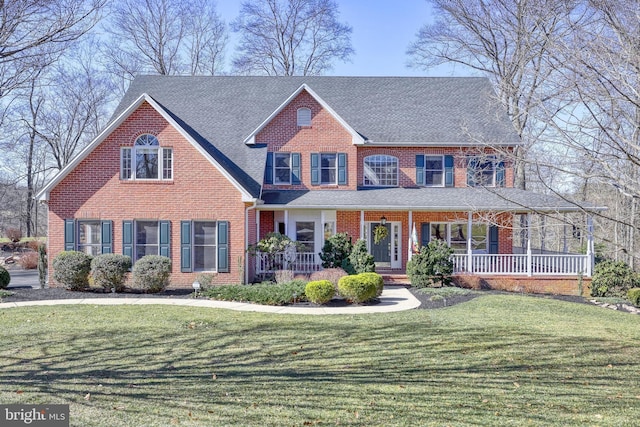 view of front of house with brick siding, covered porch, a front yard, and roof with shingles