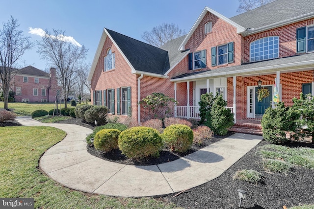 view of front of property featuring brick siding, covered porch, a front yard, and roof with shingles