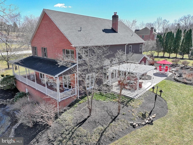 back of house with a yard, a patio, roof with shingles, and a chimney