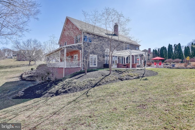 rear view of house featuring a patio, a yard, a pergola, a chimney, and brick siding