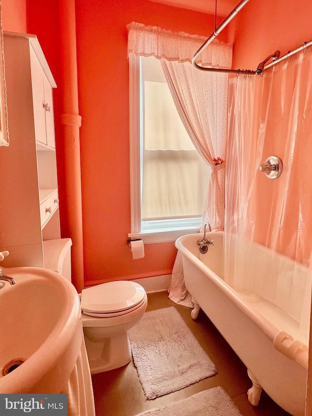 bathroom with baseboards, toilet, a shower with curtain, a freestanding tub, and a sink