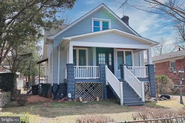 bungalow-style home featuring stairway, roof with shingles, and covered porch