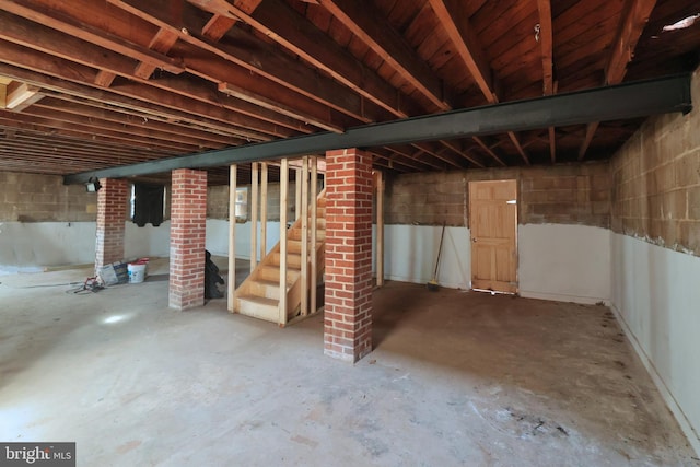 unfinished basement featuring stairway and concrete block wall