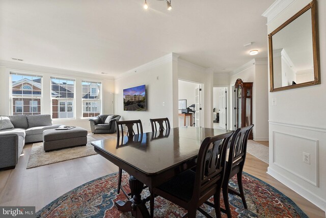 dining room featuring crown molding, a decorative wall, wood finished floors, and wainscoting