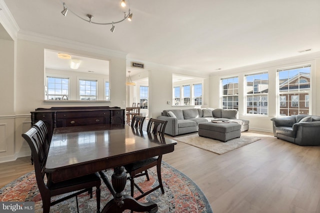 dining space with crown molding, light wood-type flooring, and wainscoting