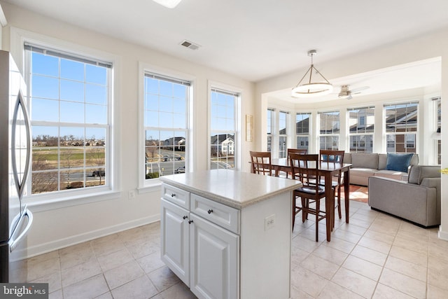 kitchen with visible vents, a kitchen island, baseboards, decorative light fixtures, and freestanding refrigerator