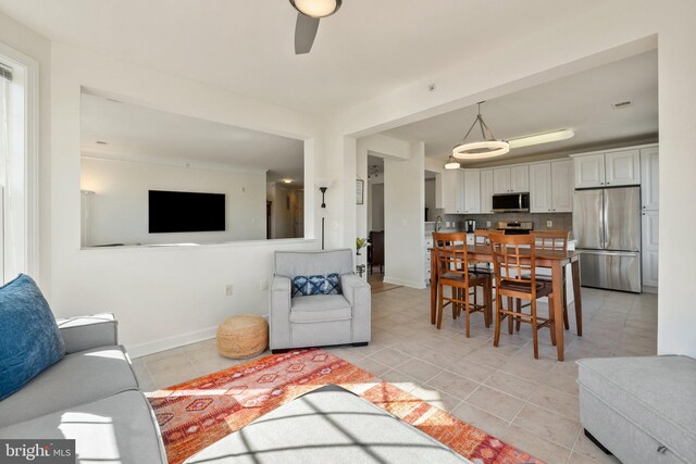 living area featuring light tile patterned floors, ceiling fan, and baseboards