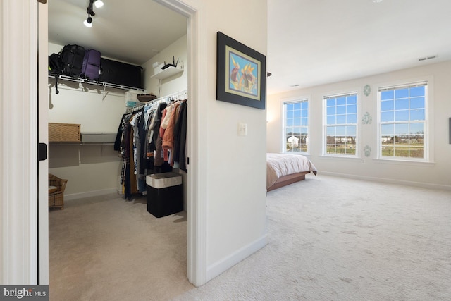 carpeted bedroom featuring a walk in closet, visible vents, track lighting, a closet, and baseboards