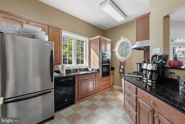 kitchen with under cabinet range hood, light floors, dark stone countertops, appliances with stainless steel finishes, and a sink