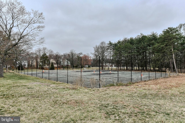 view of tennis court featuring community basketball court, fence, and a lawn