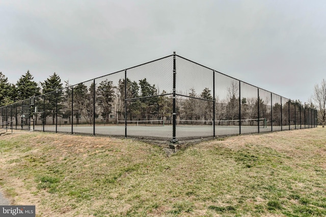 view of tennis court with a lawn and fence