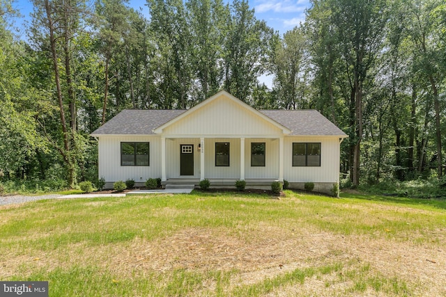 modern farmhouse style home with roof with shingles, covered porch, and a front lawn