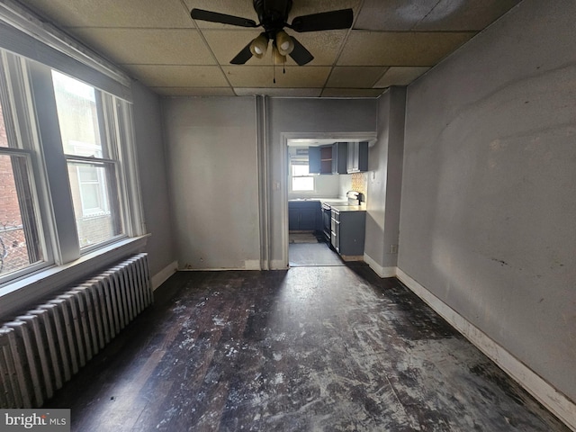 unfurnished room with baseboards, a paneled ceiling, radiator, and a ceiling fan