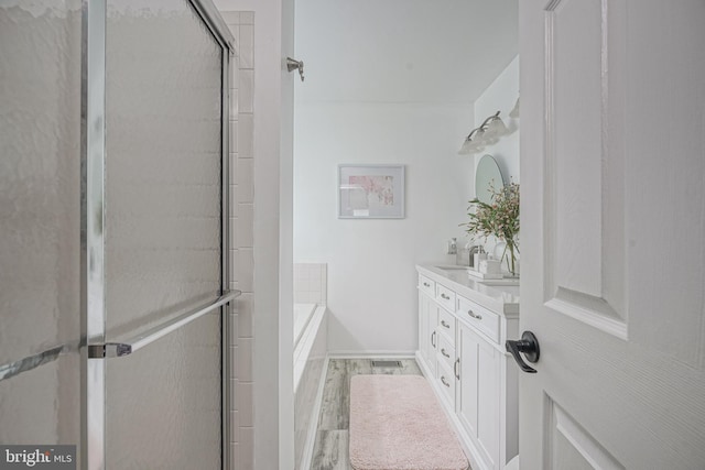 bathroom featuring wood finished floors, double vanity, a sink, an enclosed shower, and a bath