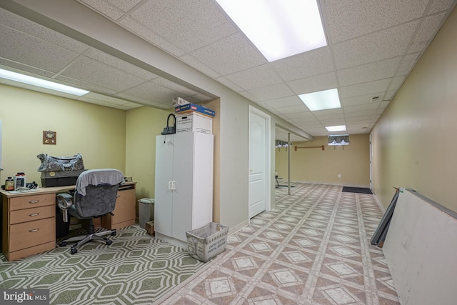 office space featuring baseboards, a paneled ceiling, and light floors