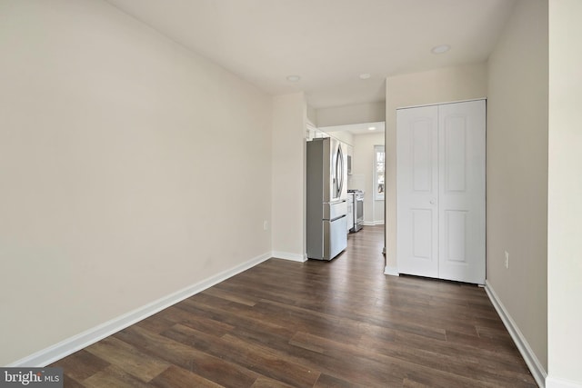 unfurnished bedroom with a closet, baseboards, dark wood-style flooring, and freestanding refrigerator