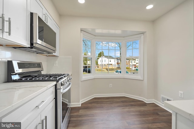 kitchen with baseboards, visible vents, dark wood finished floors, stainless steel appliances, and tasteful backsplash