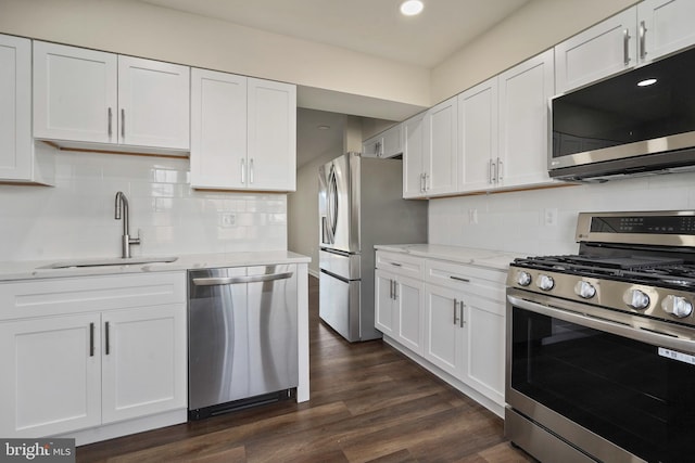 kitchen with light stone counters, dark wood-style floors, a sink, stainless steel appliances, and white cabinetry