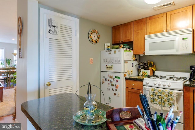 kitchen with visible vents, white appliances, dark countertops, and brown cabinetry