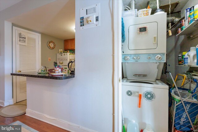 washroom with baseboards, stacked washer and clothes dryer, wood finished floors, and laundry area