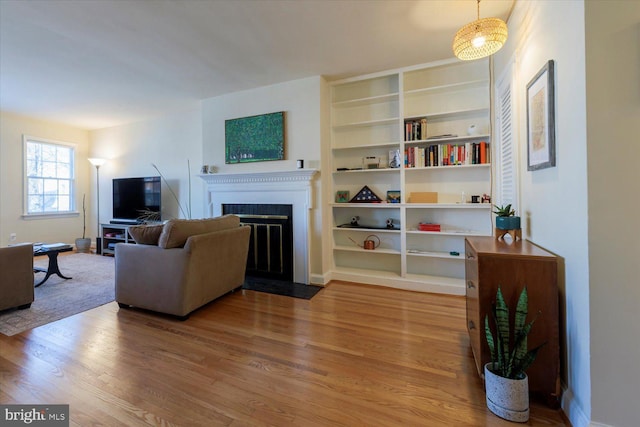 living room featuring a fireplace with flush hearth, wood finished floors, and built in features