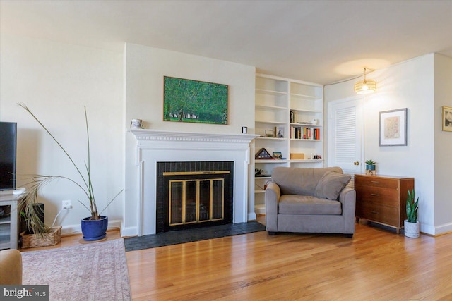 living room featuring baseboards, a fireplace with flush hearth, and wood finished floors