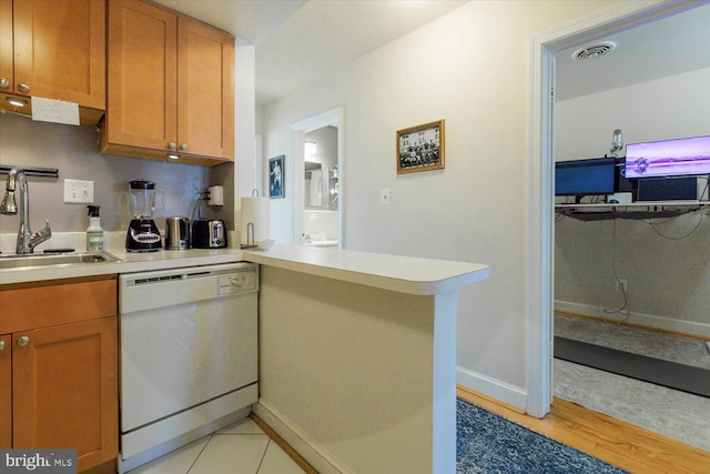 kitchen with visible vents, a sink, a peninsula, white dishwasher, and light countertops