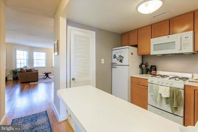 kitchen featuring white appliances, brown cabinetry, visible vents, and light countertops