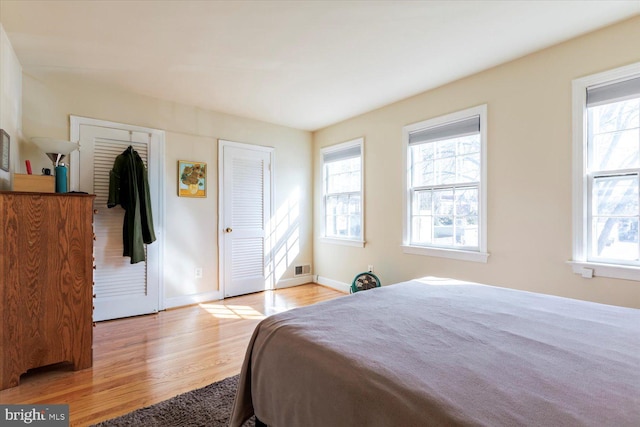 bedroom featuring visible vents, multiple windows, baseboards, and wood finished floors