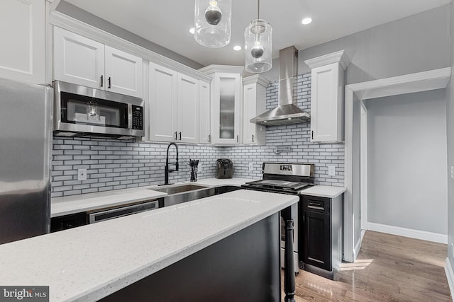 kitchen featuring light wood-style flooring, a sink, appliances with stainless steel finishes, white cabinets, and wall chimney range hood