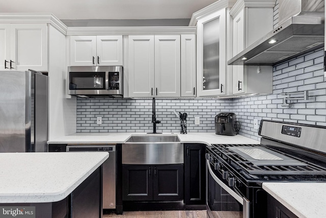 kitchen featuring a sink, appliances with stainless steel finishes, wall chimney exhaust hood, and white cabinetry