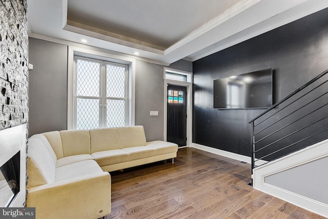 living area with wood finished floors, stairs, a stone fireplace, crown molding, and a raised ceiling