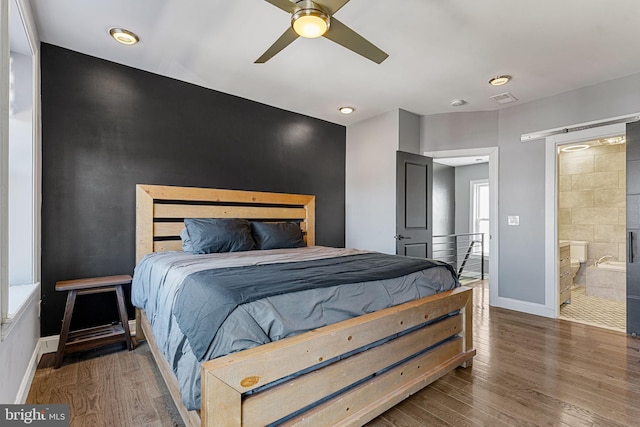 bedroom with visible vents, an accent wall, baseboards, wood finished floors, and ensuite bath