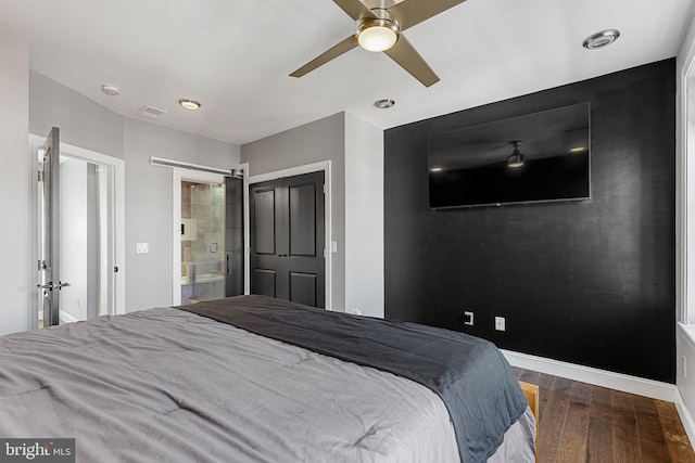 bedroom featuring a ceiling fan, wood finished floors, connected bathroom, a barn door, and baseboards