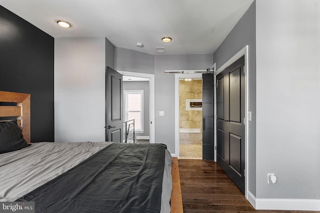 bedroom with connected bathroom, baseboards, a barn door, and dark wood-style flooring