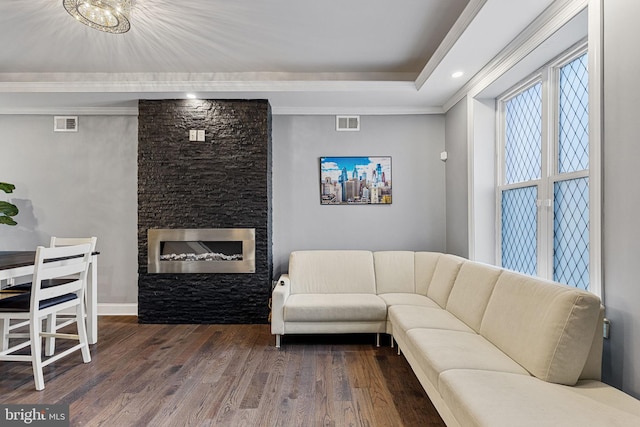 living room featuring a tray ceiling, visible vents, wood finished floors, and a fireplace