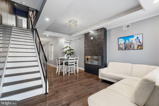 living room featuring visible vents, stairway, a tray ceiling, a stone fireplace, and wood finished floors