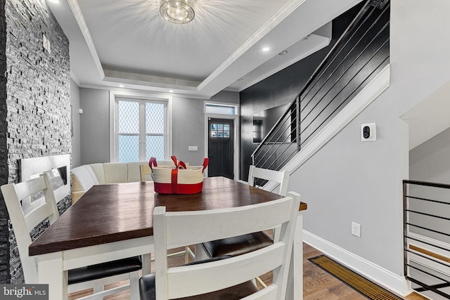 dining space featuring a raised ceiling, ornamental molding, wood finished floors, baseboards, and stairs