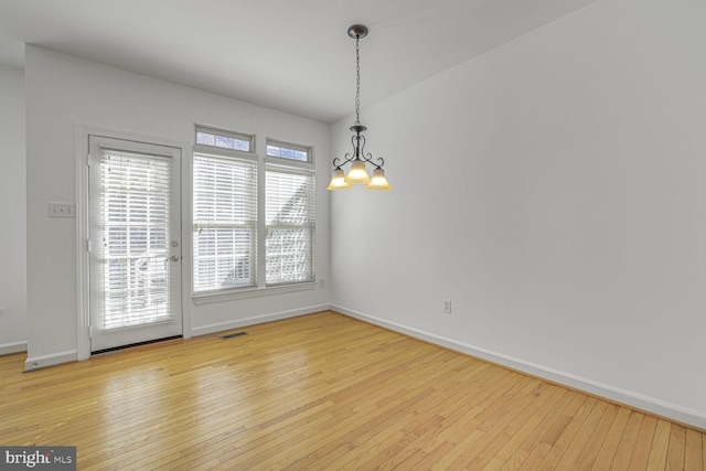 spare room with visible vents, baseboards, an inviting chandelier, and hardwood / wood-style flooring