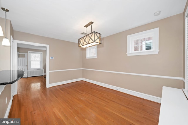 unfurnished dining area with visible vents, baseboards, wood finished floors, and radiator heating unit