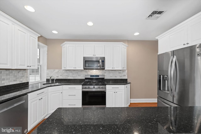 kitchen with tasteful backsplash, visible vents, white cabinets, stainless steel appliances, and a sink